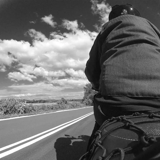 Black and white, me on a motorcycle taken from the back with the road and a cloudy sky in the background