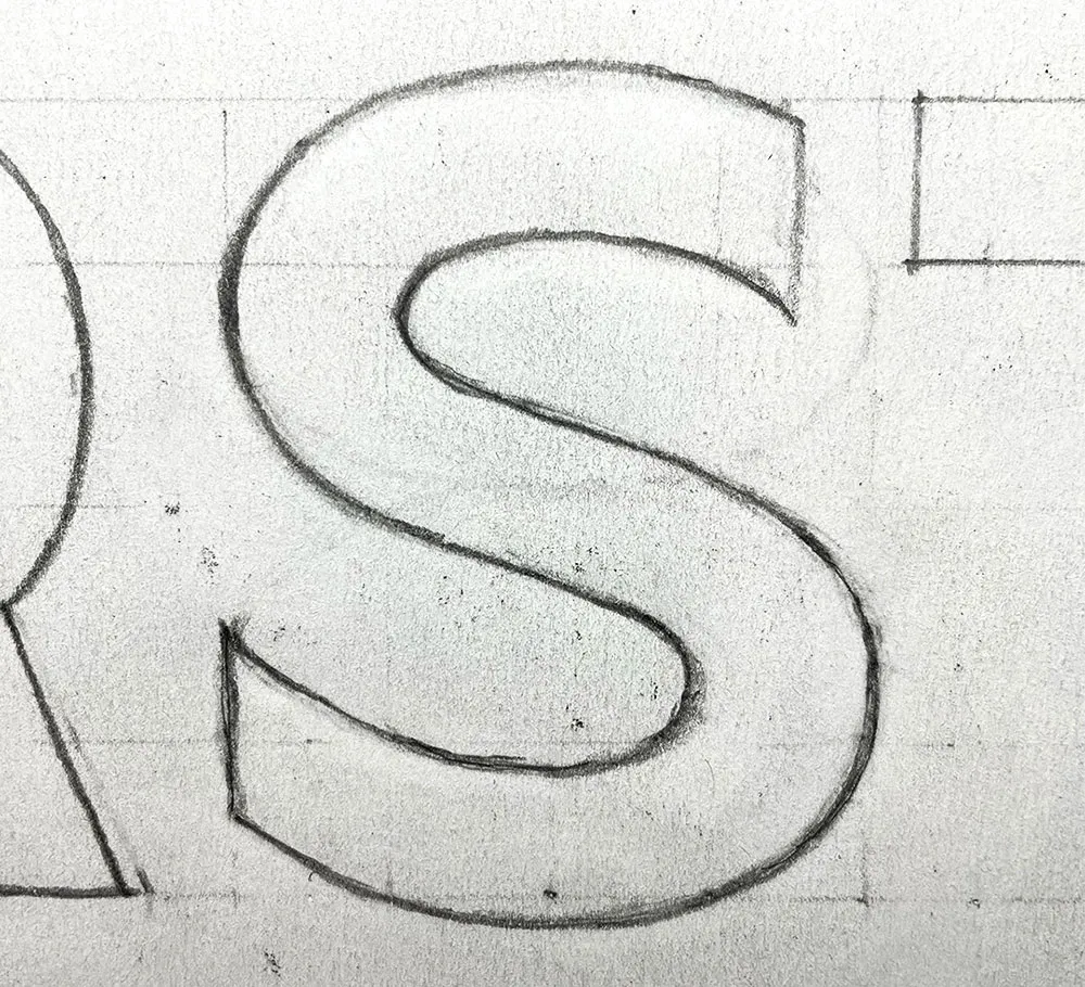 Hand drawn sans serif letter s in pencil on paper. The lines have been erased and redrawn many times so there’s a lot of smudges. The paper is white but it’s almost a light gray from all the erasing. Parts of other letters can be seen on the edges.