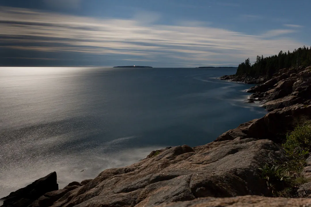 Long exposure at night looking out to sea with the rocky shore in the foreground.